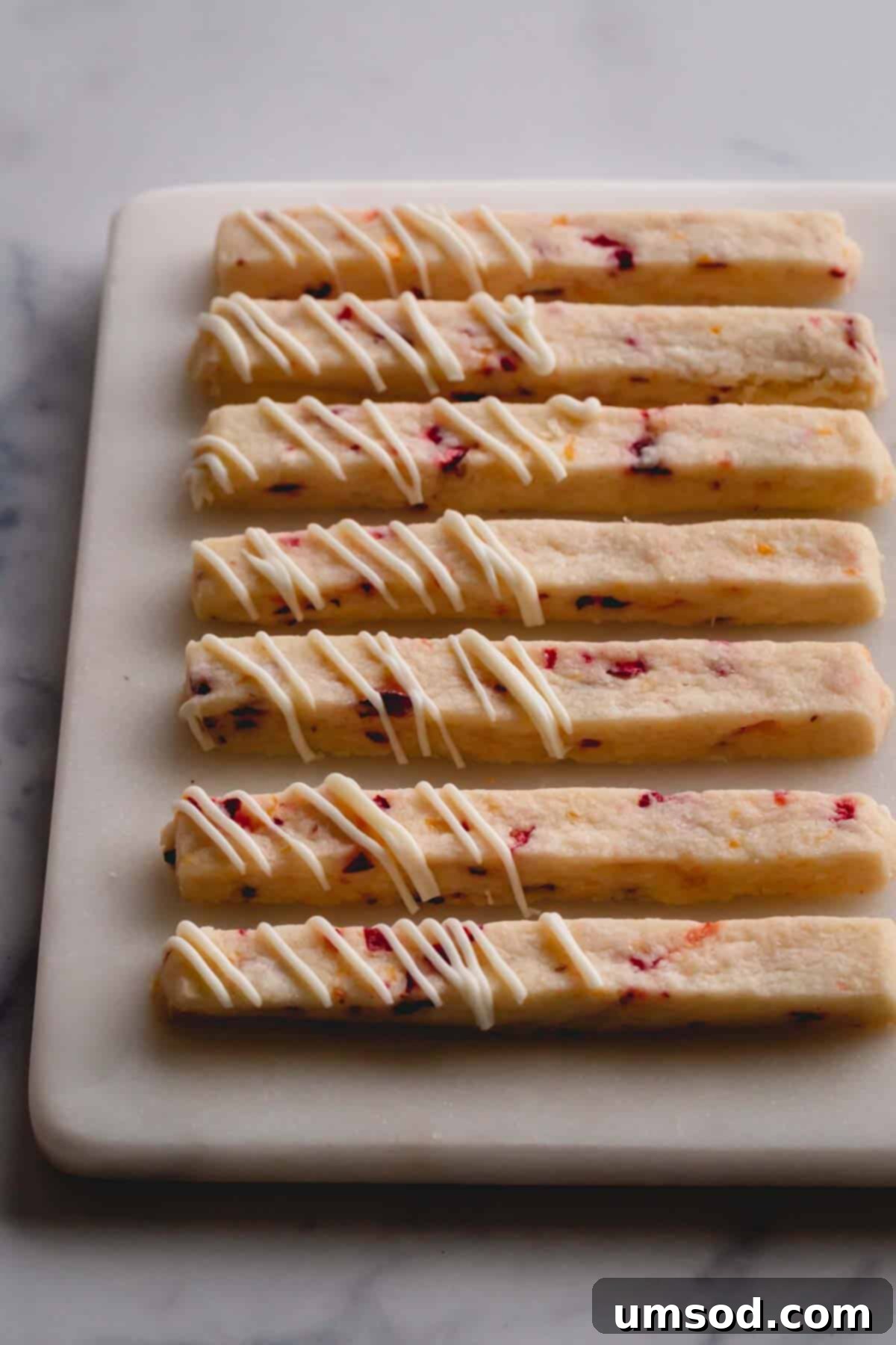 close-up photo of orange cranberry shortbread cookie sticks on a wooden cutting board, garnished with fresh cranberries and orange slices.