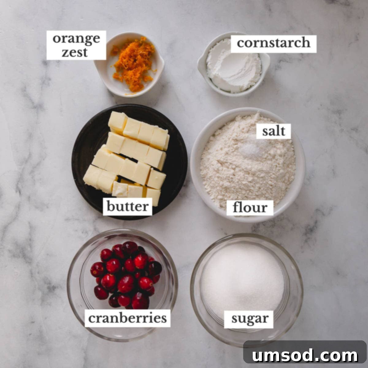 overhead shot of all ingredients for cranberry orange shortbread cookies laid out on a white surface, including flour, sugar, butter, cranberries, and oranges.