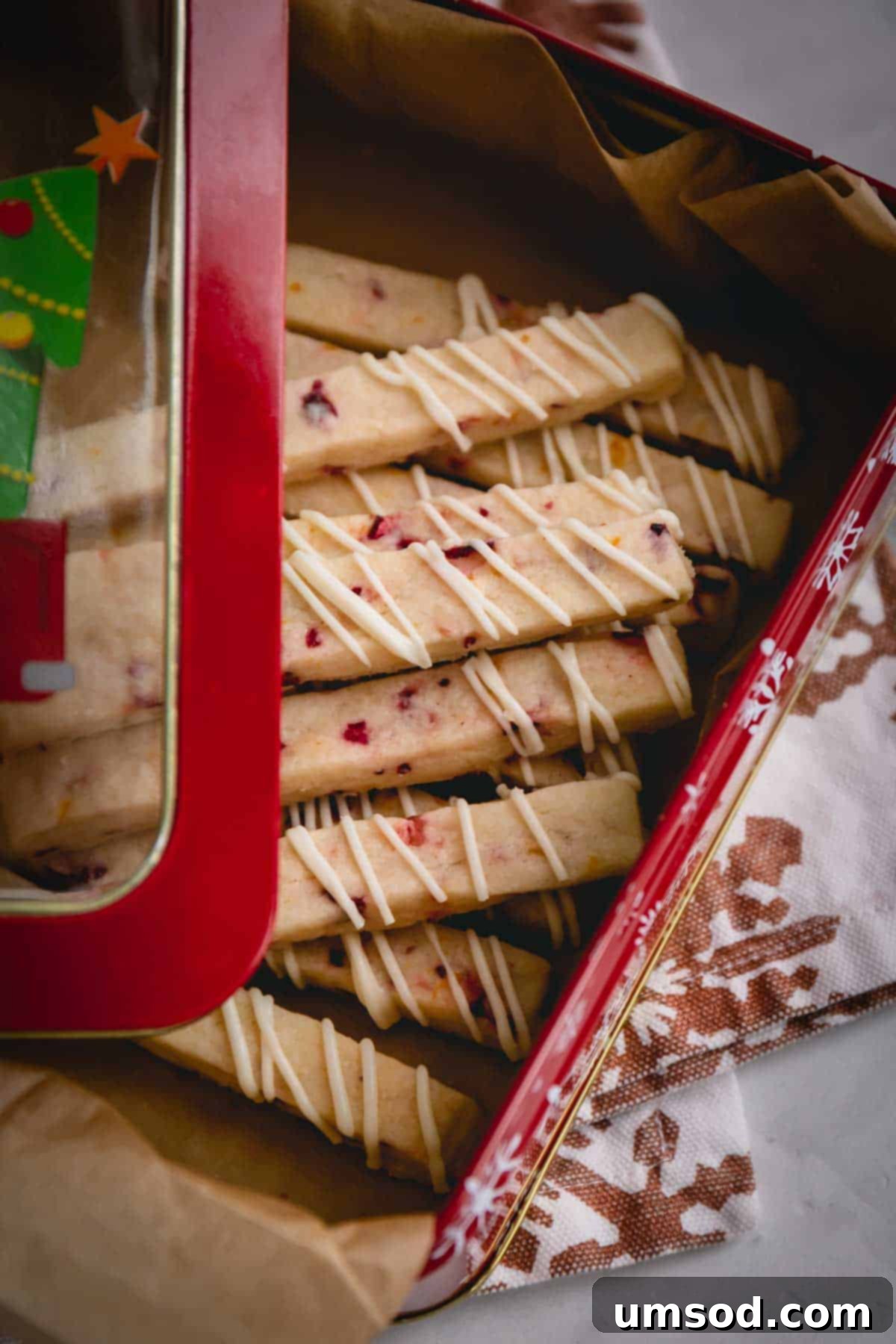 a decorative tin filled with golden cranberry orange shortbread sticks, perfect for gifting.