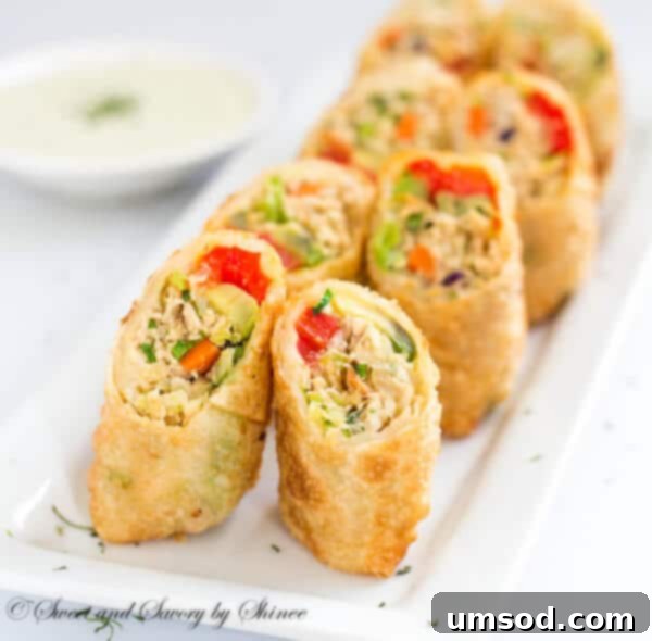Freshly fried, golden chicken avocado egg rolls piled high in a bowl, with cilantro dipping sauce on the side.