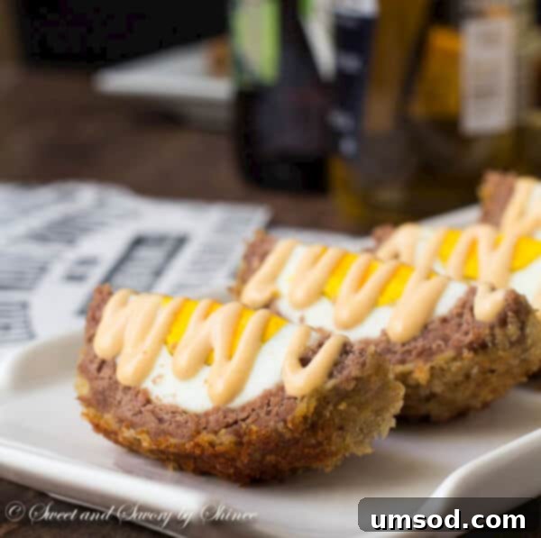 Close-up of a perfectly sliced Scotch egg quarter, showing the layered crispy exterior, seasoned meat, and firm egg yolk, with a dollop of tangy mustard sauce.