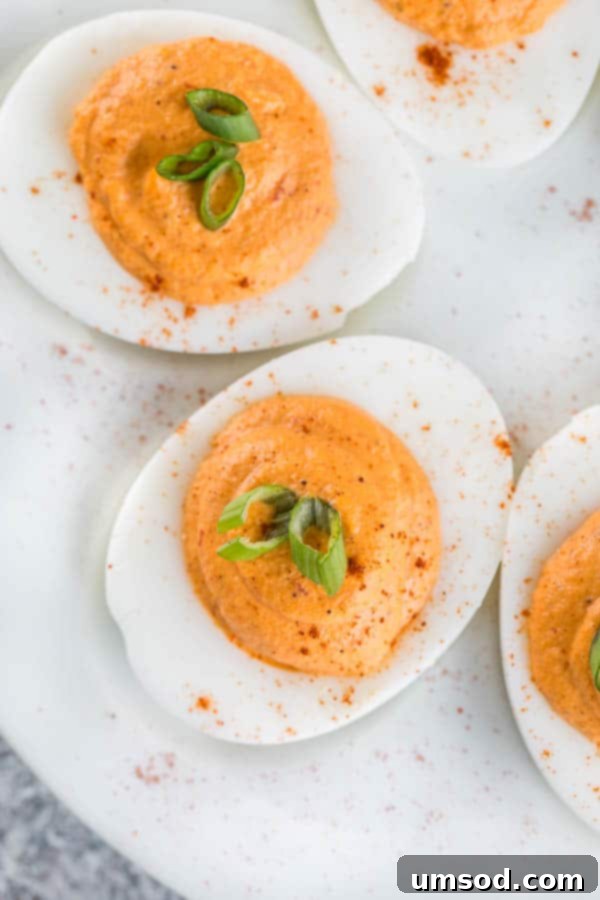 Preparing creamy filling for Roasted Red Pepper Deviled Eggs, showing roasted red peppers being added.