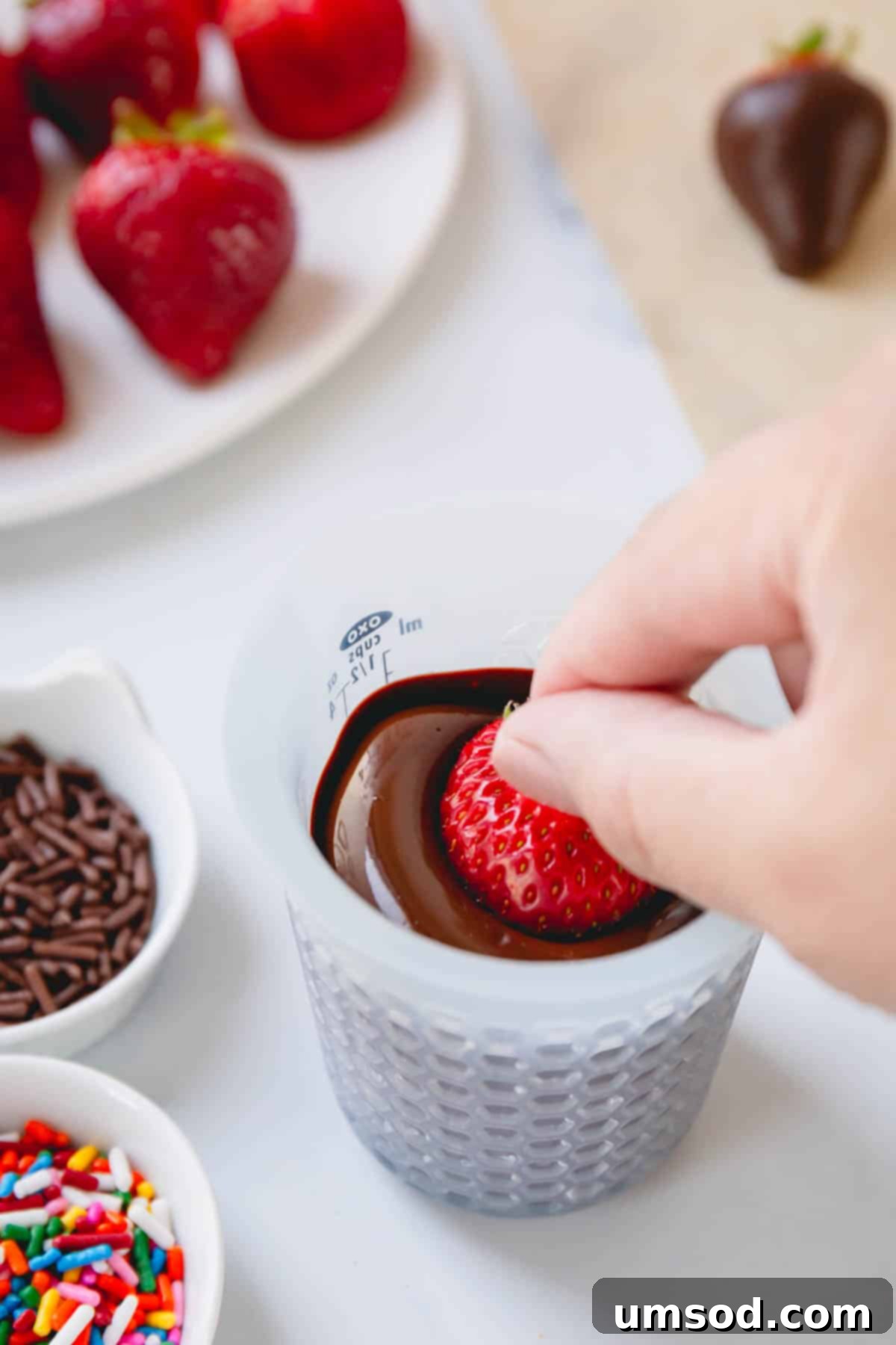 A hand dipping a clean strawberry into melted chocolate.