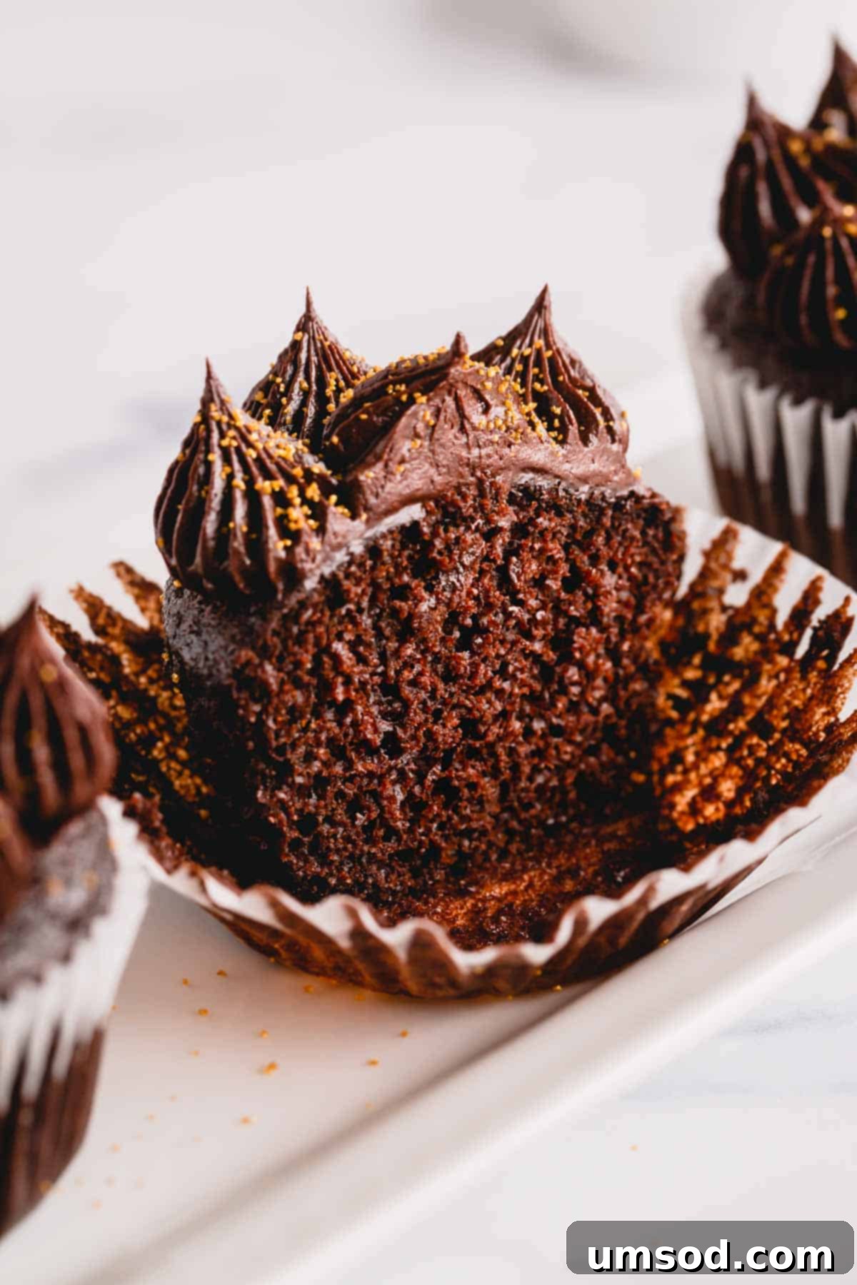 A perfectly baked, moist ultimate chocolate cupcake, half-eaten and topped with smooth chocolate frosting, resting in its liner.