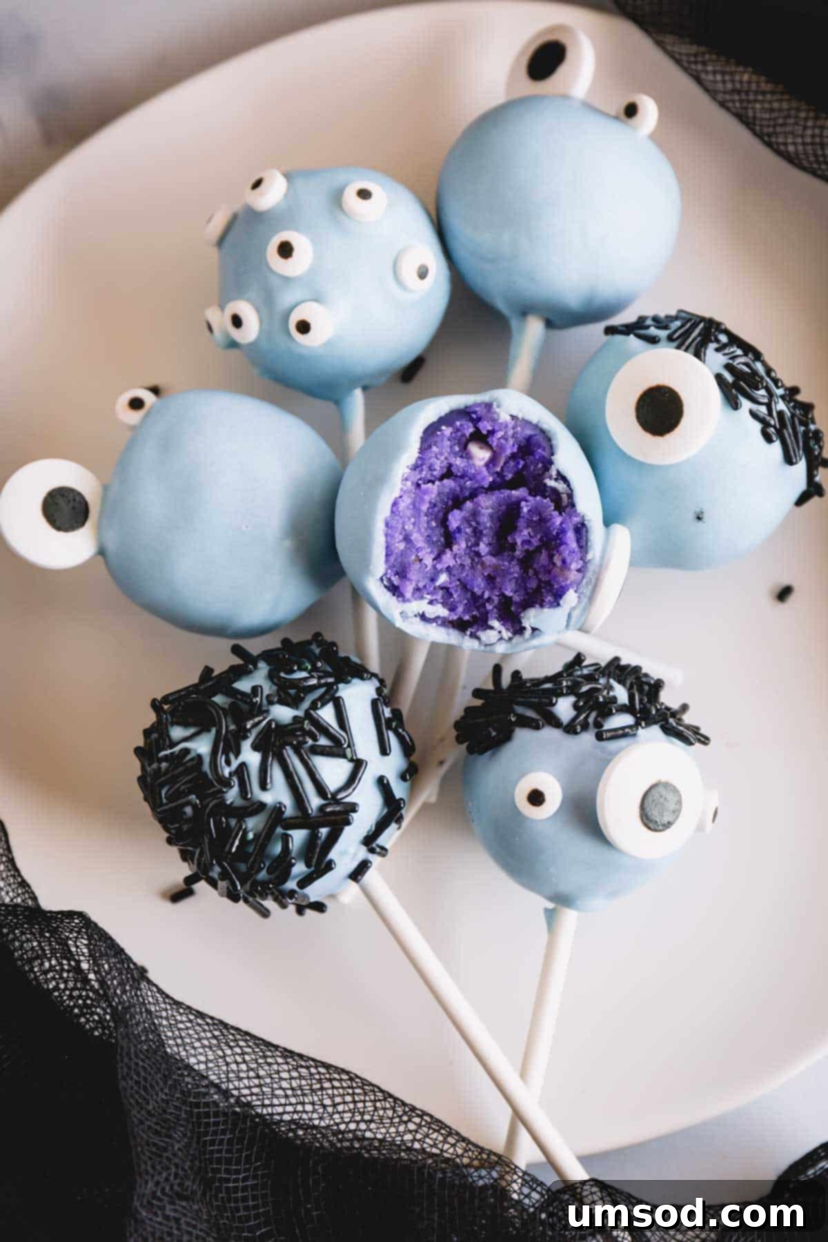 Ghoulishly Good Cake Pops 11 Blue monster cake pops with various candy eyes and sprinkle hair, one with a bite missing.