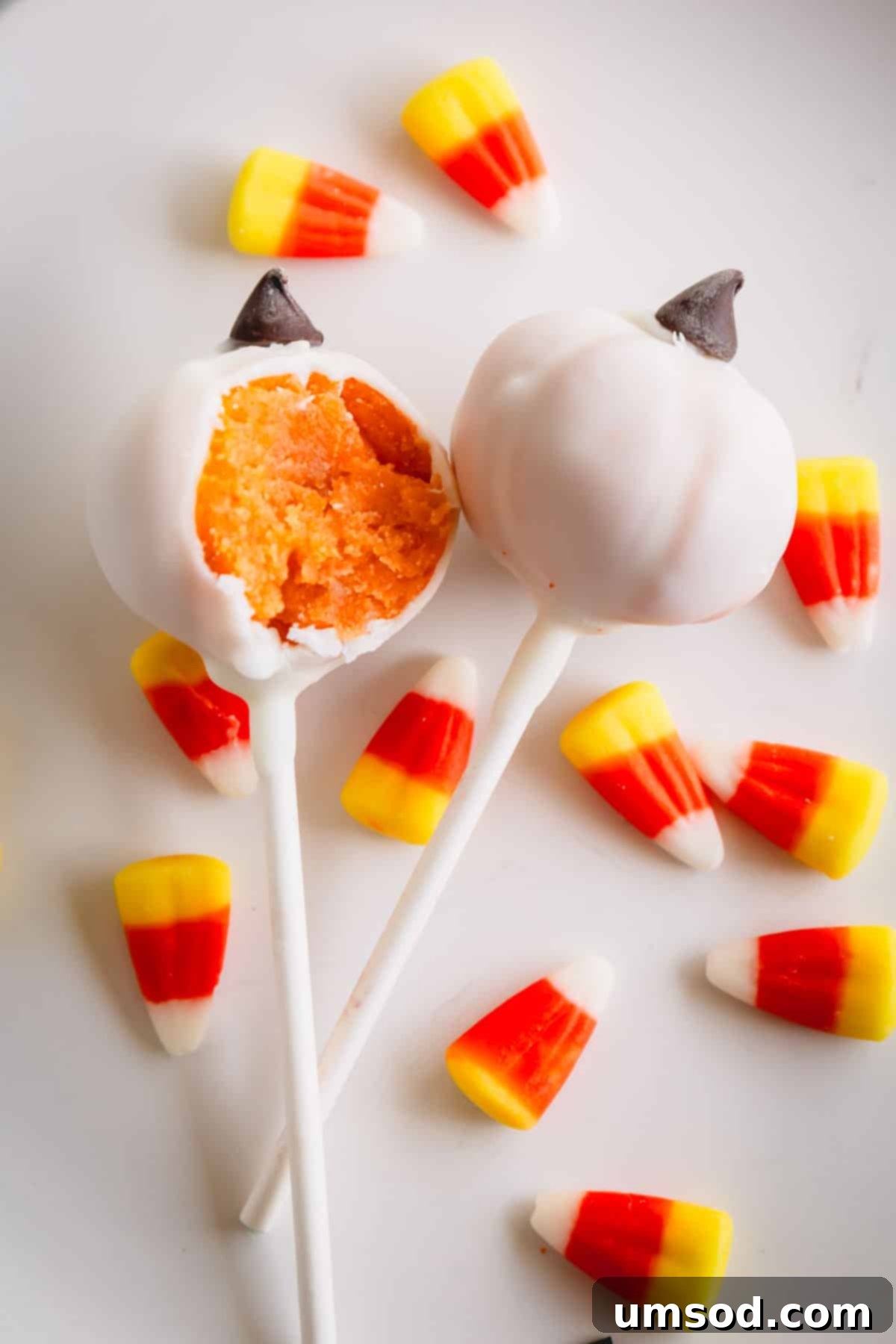 Ghoulishly Good Cake Pops 8 Two white pumpkin cake pops, one with a bite taken out, surrounded by festive candy corn.