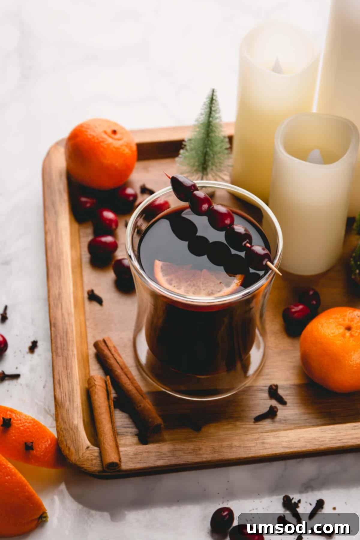 A festive close-up of mulled wine in a glass, garnished with fresh cranberries and a vibrant orange slice.