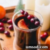 Mulled wine in a glass garnished with fresh cranberries and slice of orange.