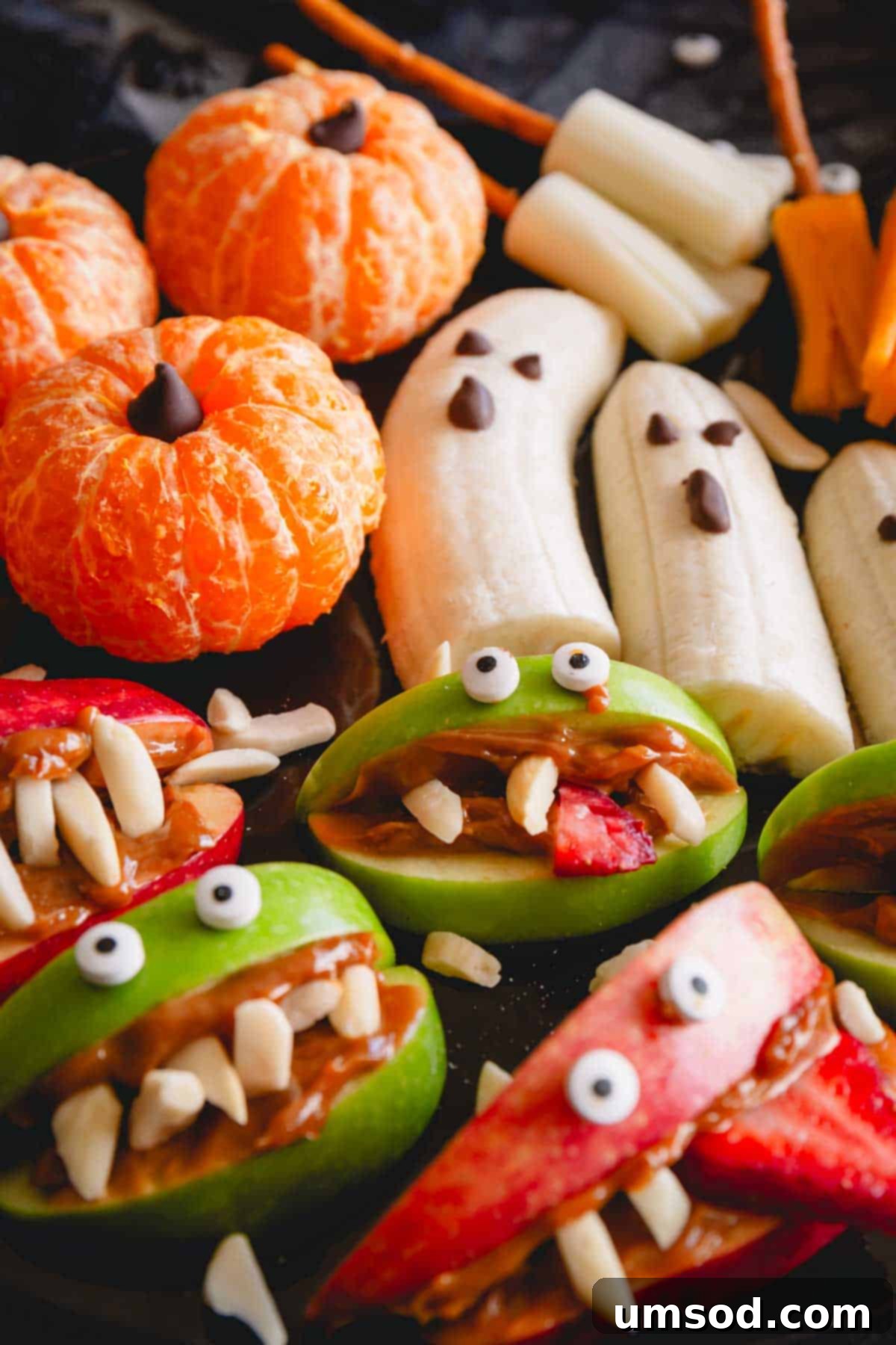 Close-up of pumpkin oranges, banana ghosts, and apple monster mouths creatively arranged on a Halloween-themed snack board.