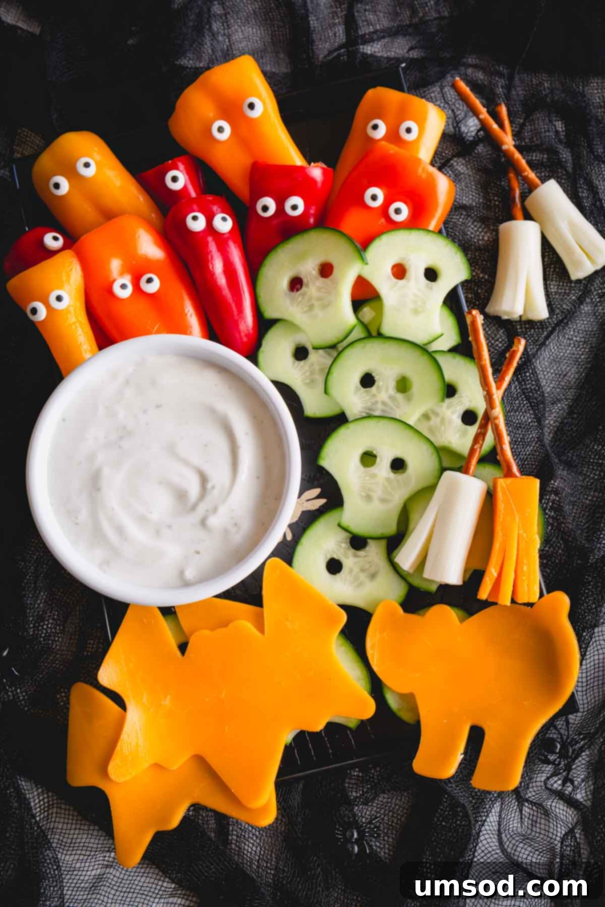 Close-up of creatively prepared Halloween snacks: ghost bell peppers, mummy cucumbers, cheese broomsticks, and festive cheese shapes with dip.