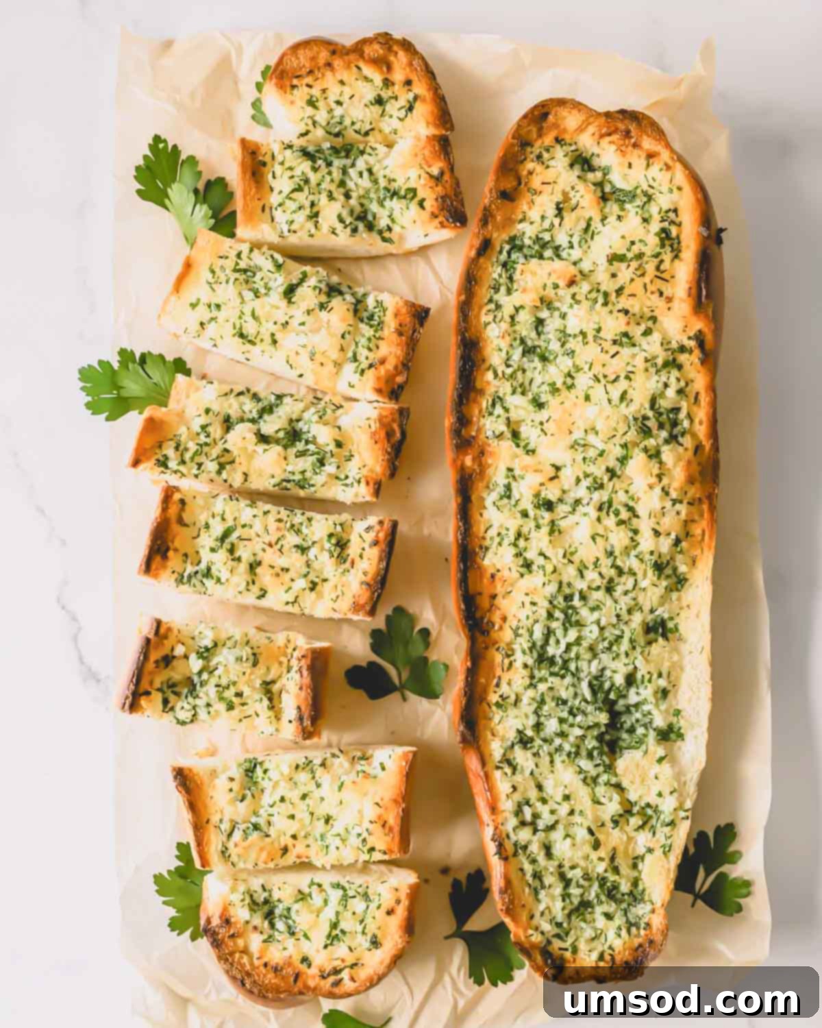 Perfect Garlic Bread in Minutes 2 Two loaves of garlic bread topped with an herbed butter spread with one sliced into pieces.