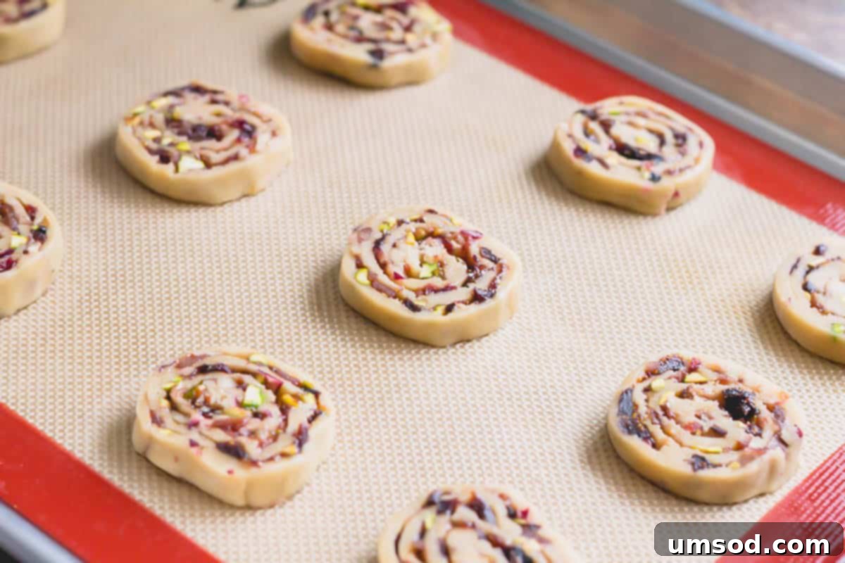 Raw pinwheel cookies, perfectly sliced and arranged on a baking sheet lined with a silicone mat, ready for the oven.