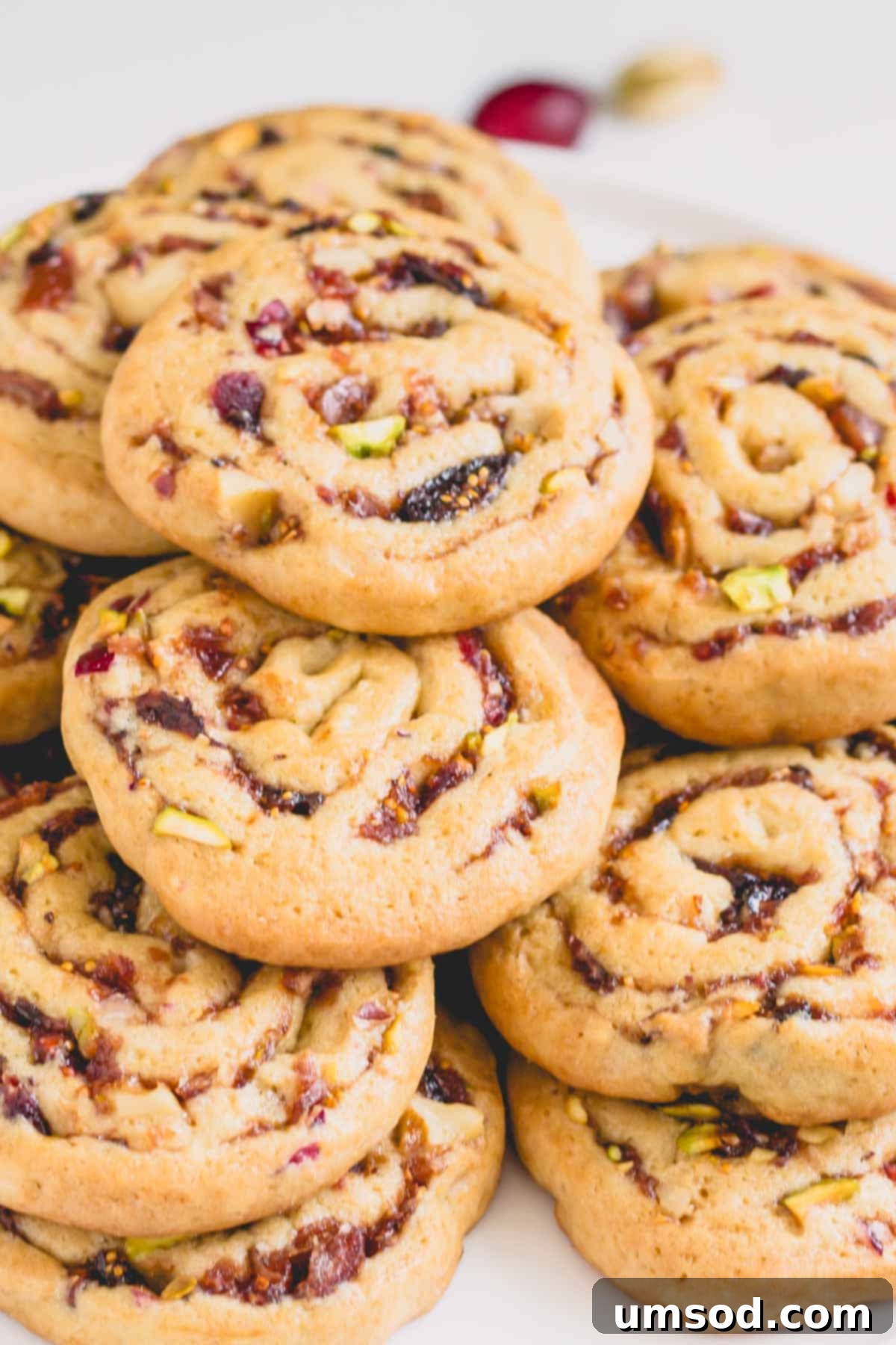 A stack of perfectly baked fig, cranberry, and date pinwheel cookies, showing their golden edges and swirled centers.