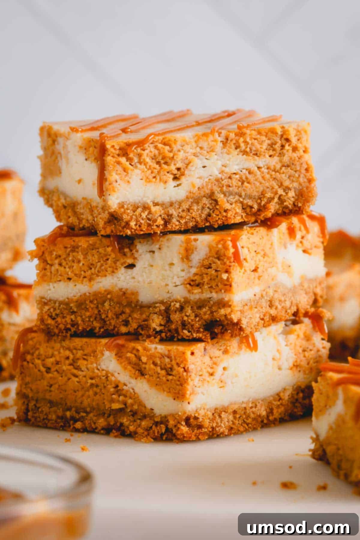 A stack of three perfect pumpkin cheesecake bars with a golden graham cracker crust, ready to be enjoyed.