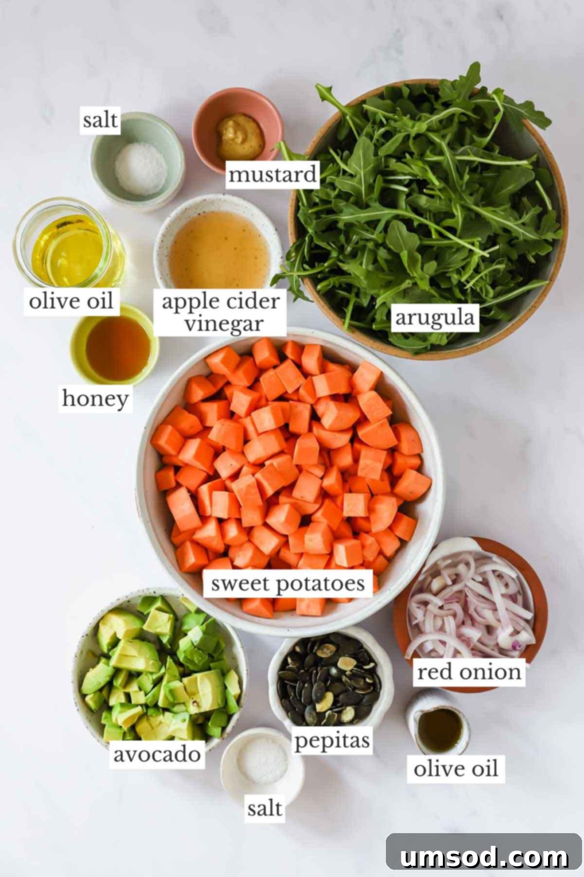 Sunshine Sweet Potato Salad 4 A colorful array of fresh ingredients for sweet potato salad, including roasted sweet potatoes, arugula, avocado, red onion, and a jar of homemade vinaigrette.