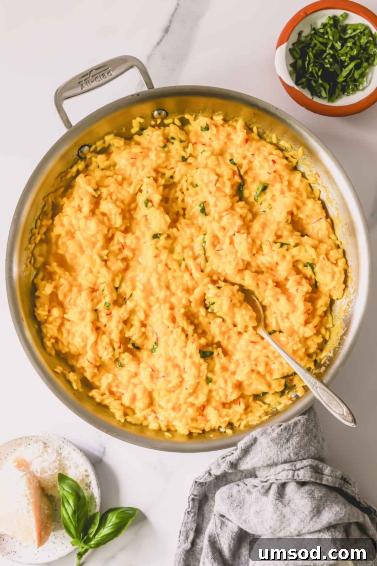 A pan filled with beautifully cooked saffron risotto, garnished with fresh herbs, with a wooden spoon resting in the dish.