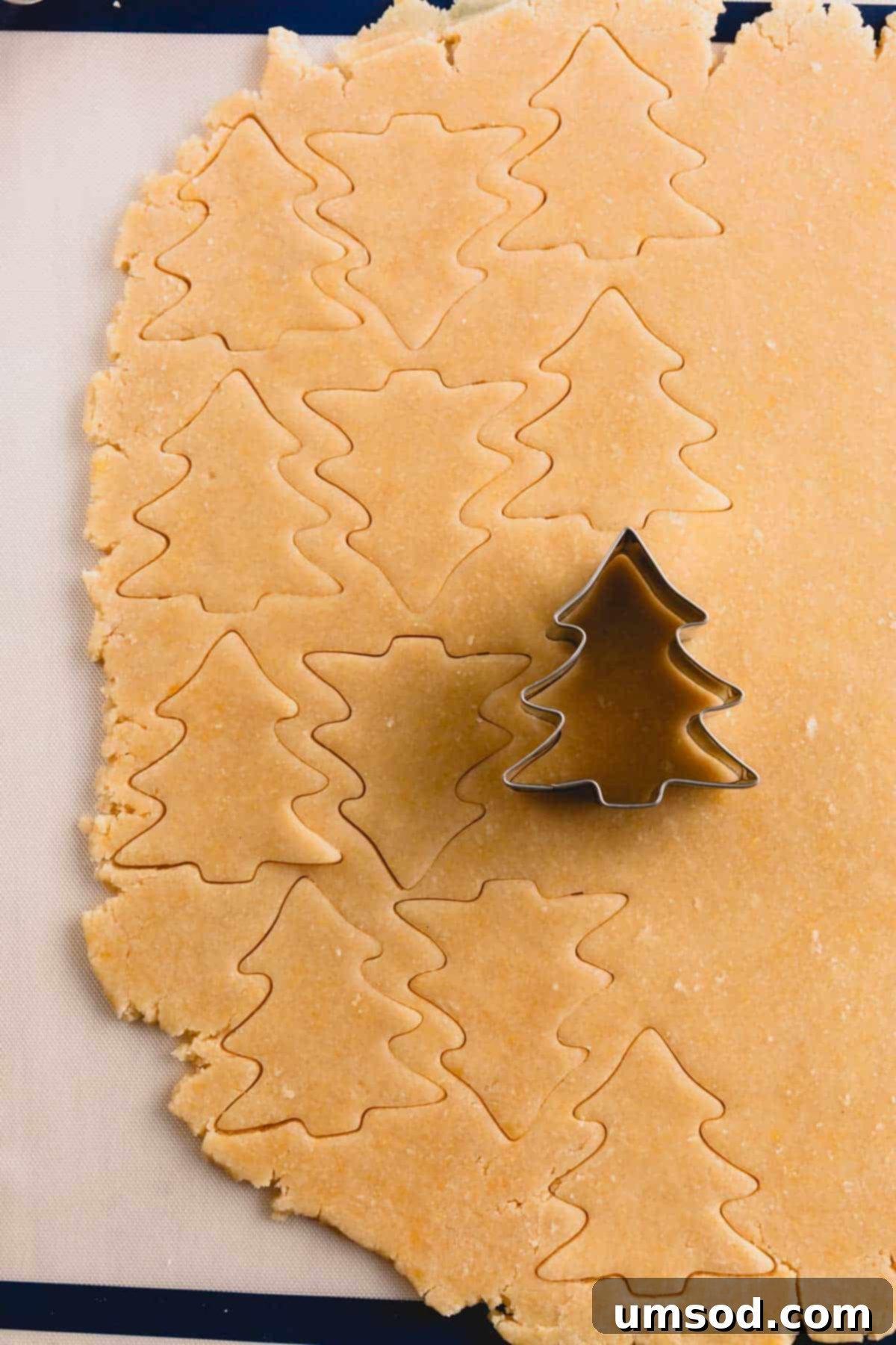 Sugar cookie dough being precisely cut with a Christmas tree cookie cutter, ready for baking.
