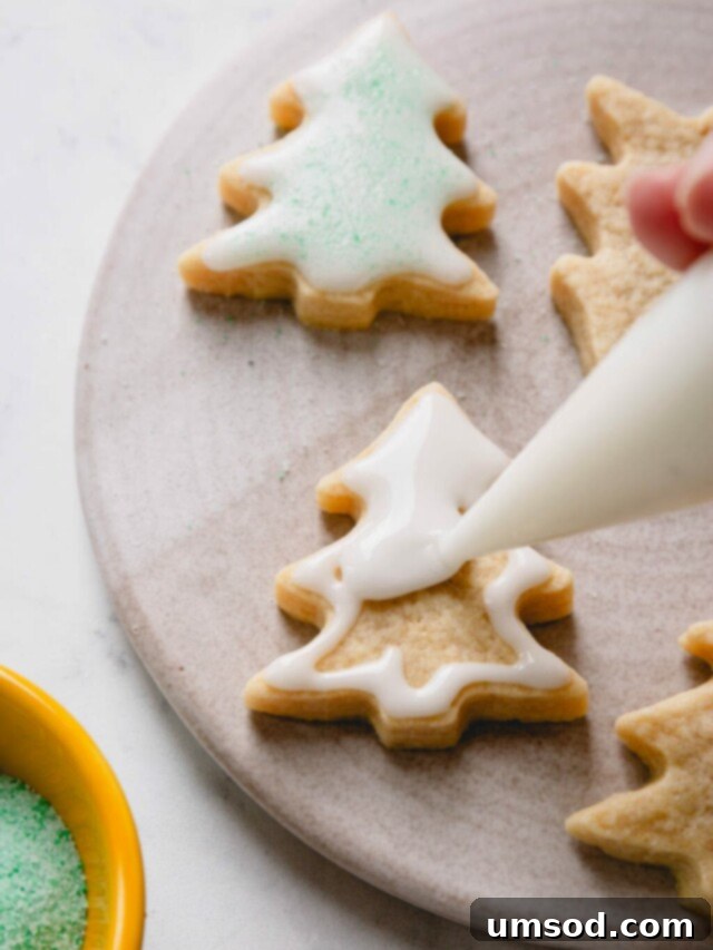Christmas tree-shaped sugar cookies in the process of being flooded with royal icing to create a smooth, even base for decoration.