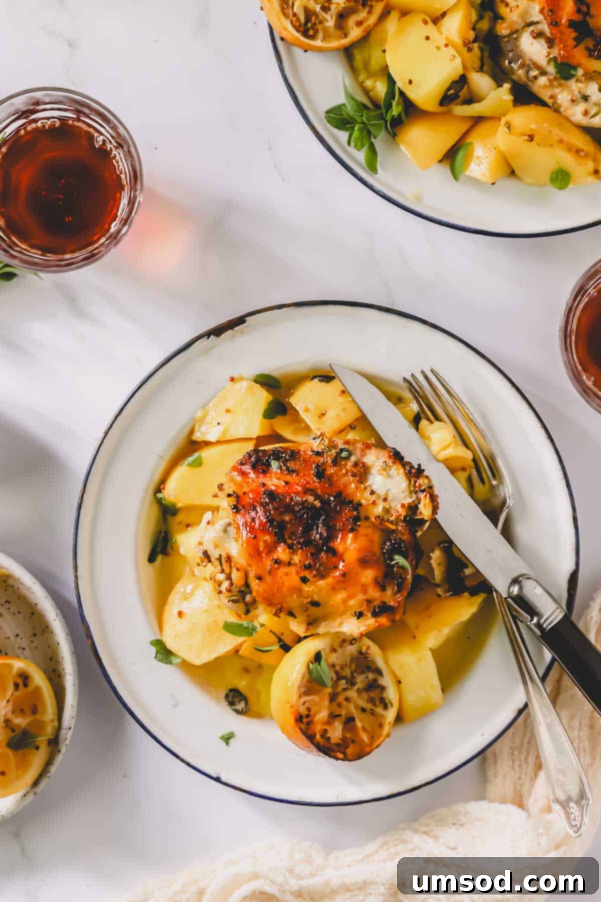 A beautifully plated serving of Greek lemon chicken and potatoes, accompanied by a knife and fork.