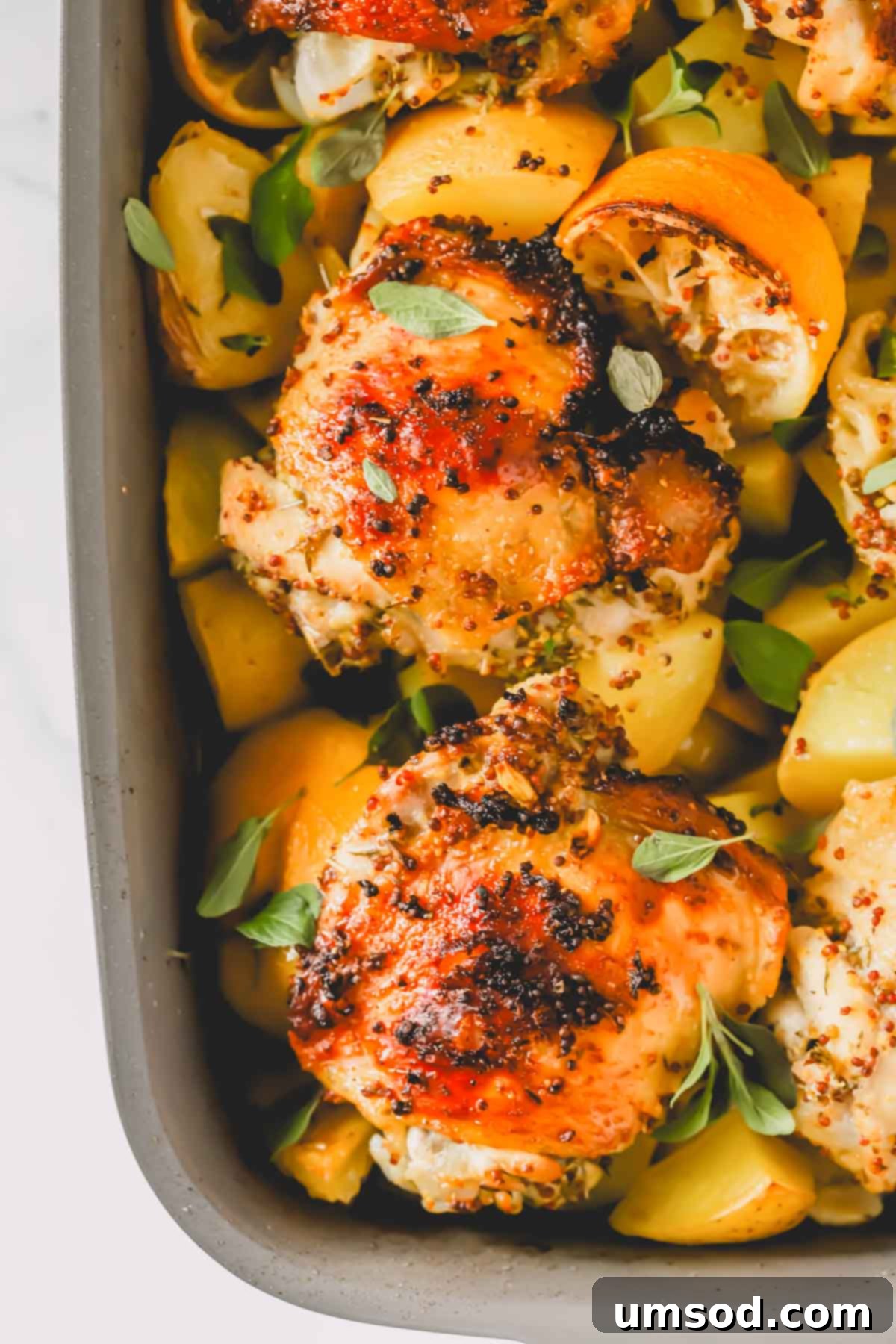 A baking dish filled with roasted Greek lemon chicken and potatoes, adorned with lemon halves.