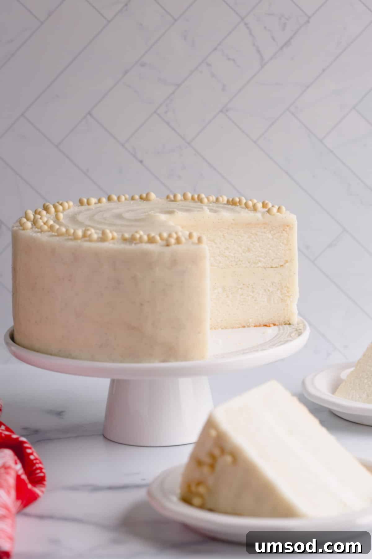 Fluffy White Cake Perfection 13 A fully assembled classic white cake, frosted with vanilla buttercream, with a perfect slice resting on a plate beside it.