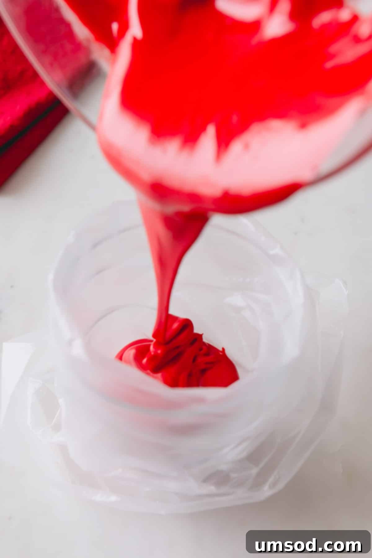 Red royal icing being poured into a piping bag, demonstrating proper technique.