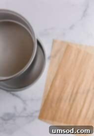 Effortless Parchment Circles for Round Cake Pans 3 Two stacked round cake pans alongside a roll and a sheet of parchment paper, demonstrating the necessary tools for cutting parchment circles.