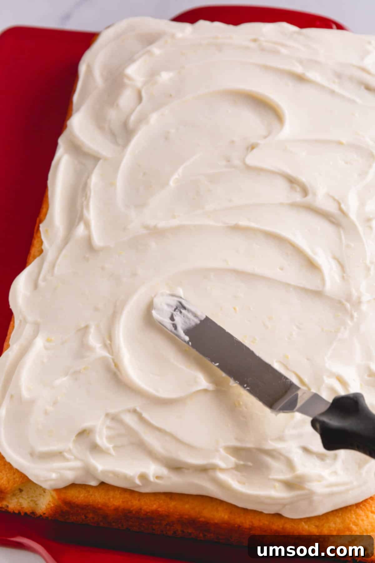 A lemon sheet cake being frosted with lemon cream cheese frosting.