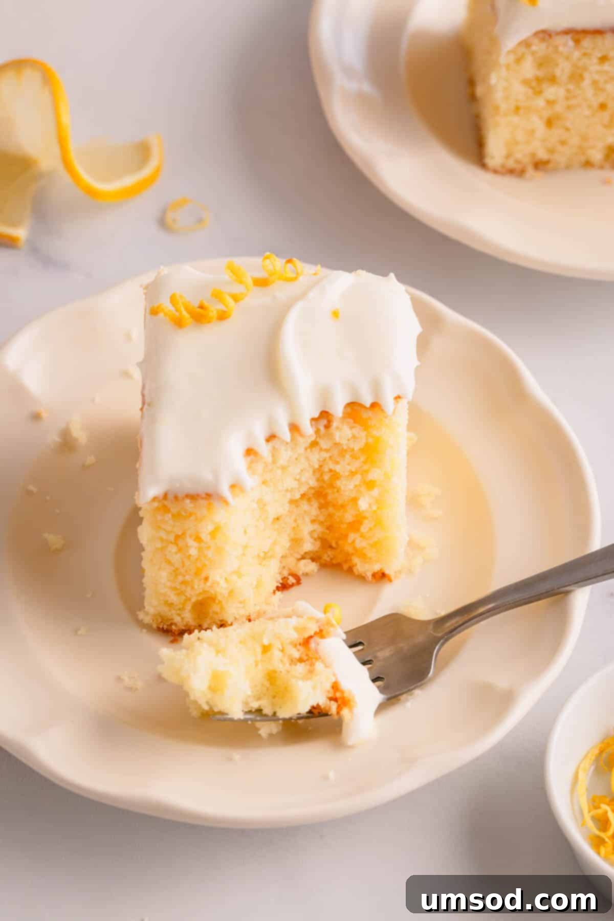 A slice of frosted lemon sheet cake on a plate with a fork holding a bite.