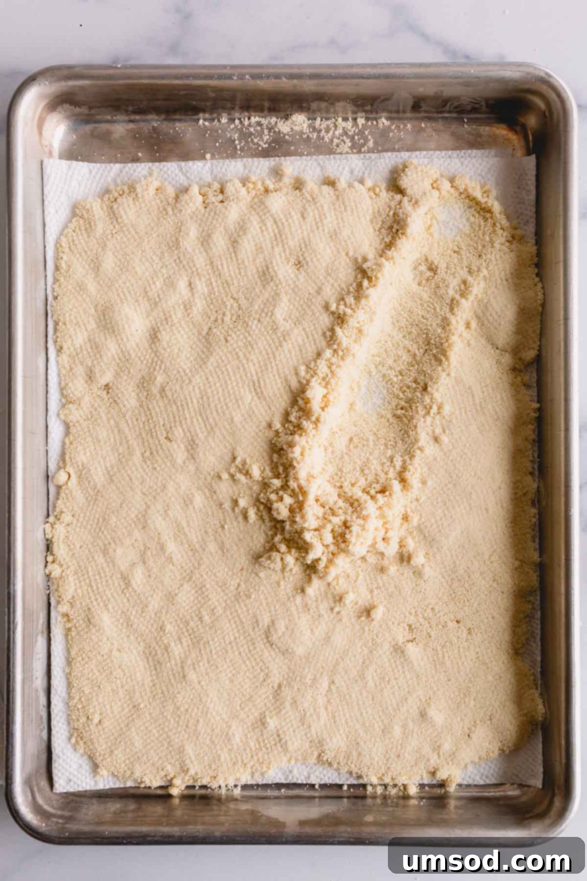 Revive Your Oily Almond Flour 8 A layer of almond flour on a baking sheet lined with paper towel, now fluffed with a spoon after drying.
