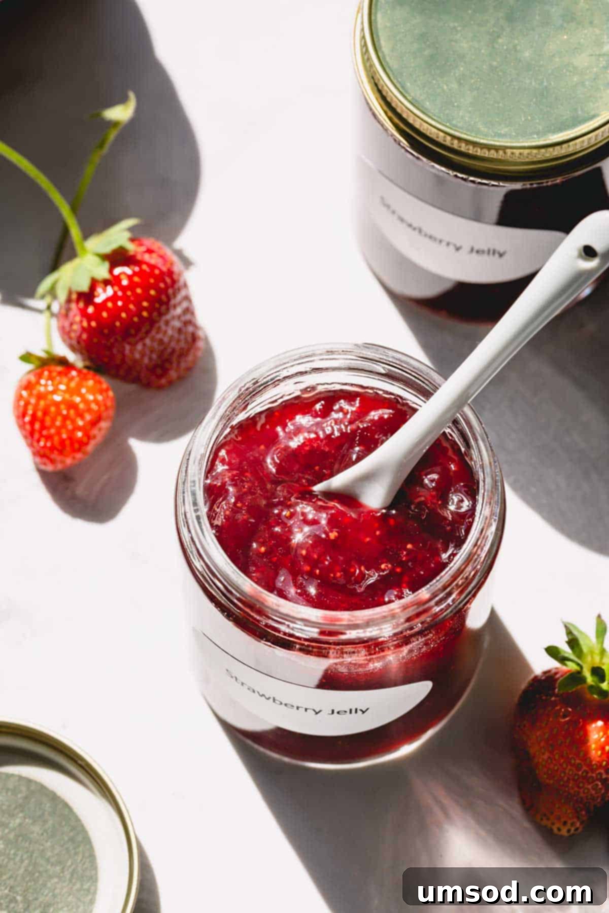 Homemade strawberry jam in a charming glass jar, accompanied by a spoon, sitting on a rustic wooden surface.