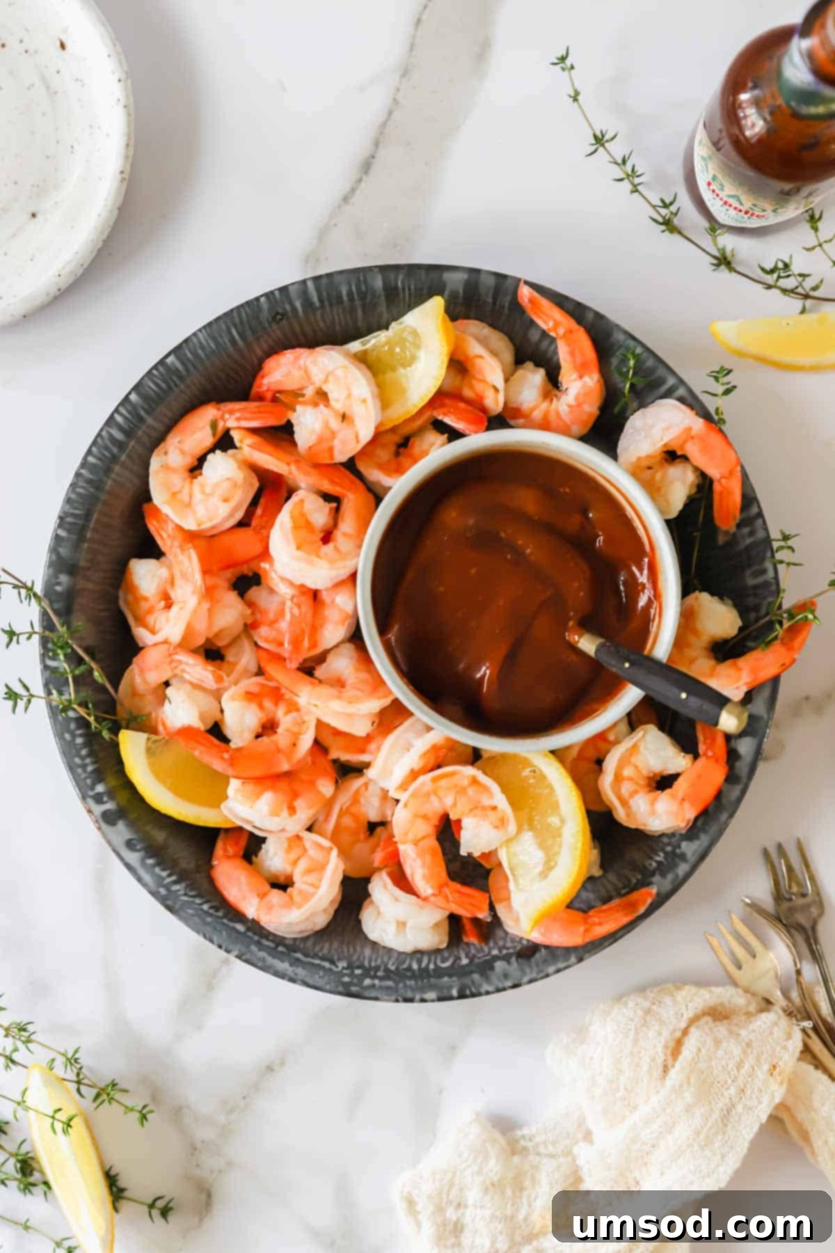 A beautifully arranged bowl of cocktail shrimp with a vibrant red cocktail sauce in the center, garnished with fresh lemon.