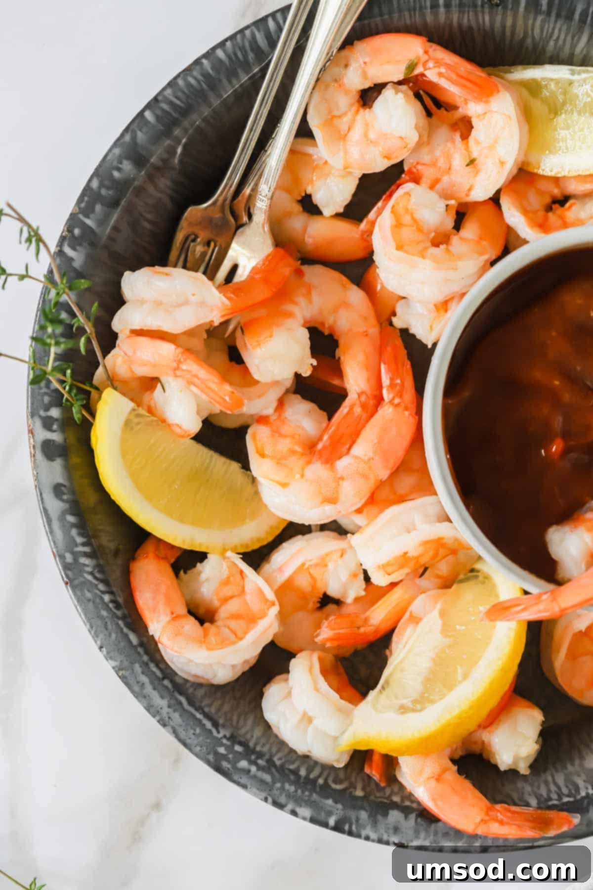 A close-up shot of cocktail shrimp artfully arranged in a bowl, with vibrant lemon wedges and a small dish of red cocktail sauce for dipping.