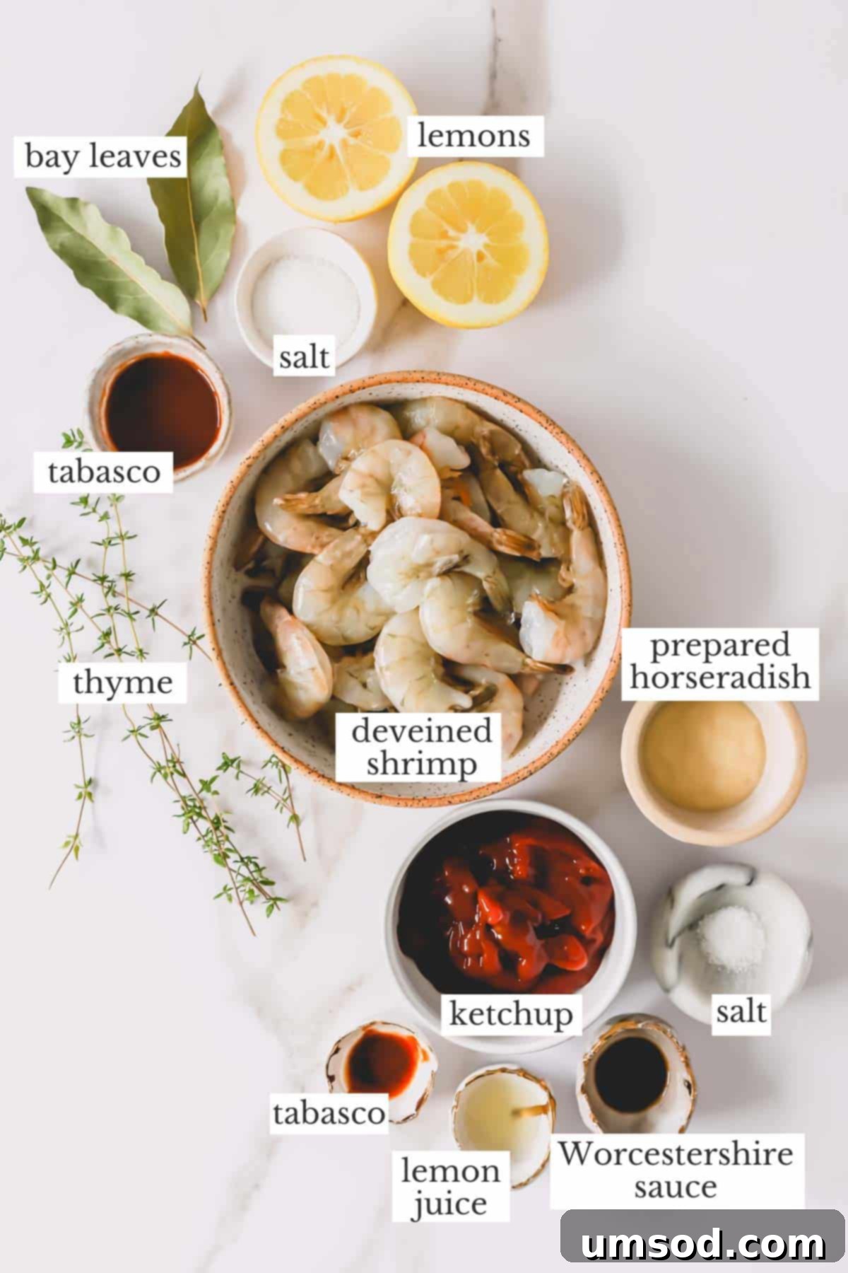 A colorful array of fresh ingredients laid out on a wooden surface, including jumbo shrimp, lemons, fresh herbs, and various bottles and jars for the cocktail sauce.