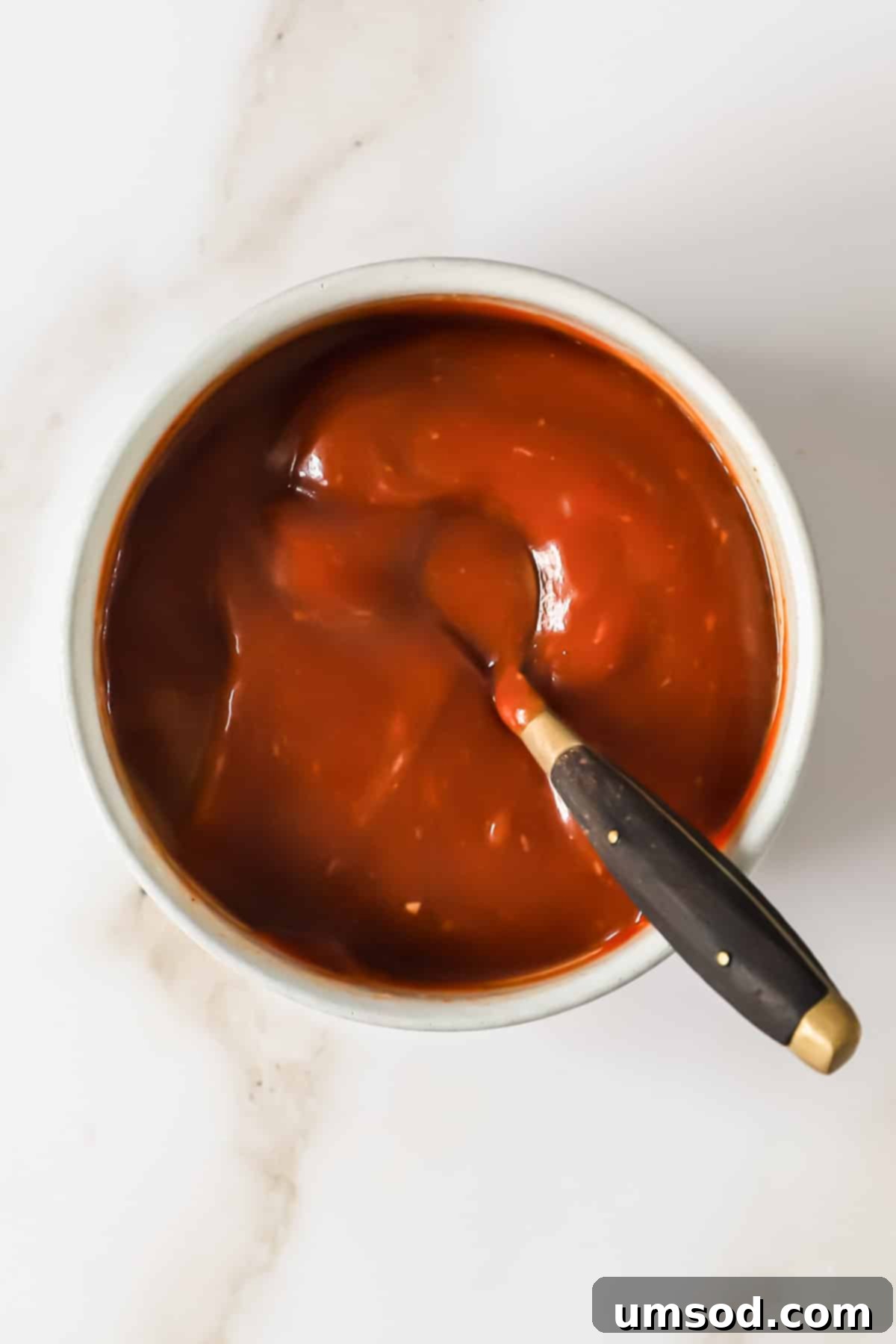 A small glass bowl brimming with bright red homemade cocktail sauce, with a silver spoon resting in it.