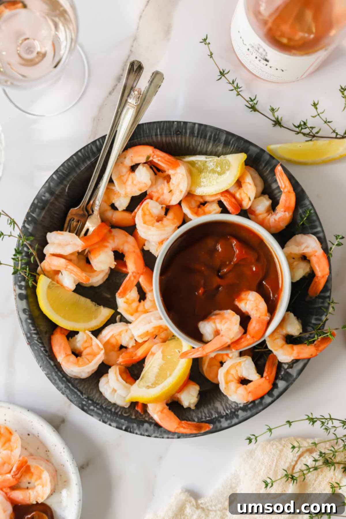 A generous bowl of beautifully arranged shrimp cocktail, with a central dish of vibrant cocktail sauce. Two shrimp are already dipped and waiting to be enjoyed.