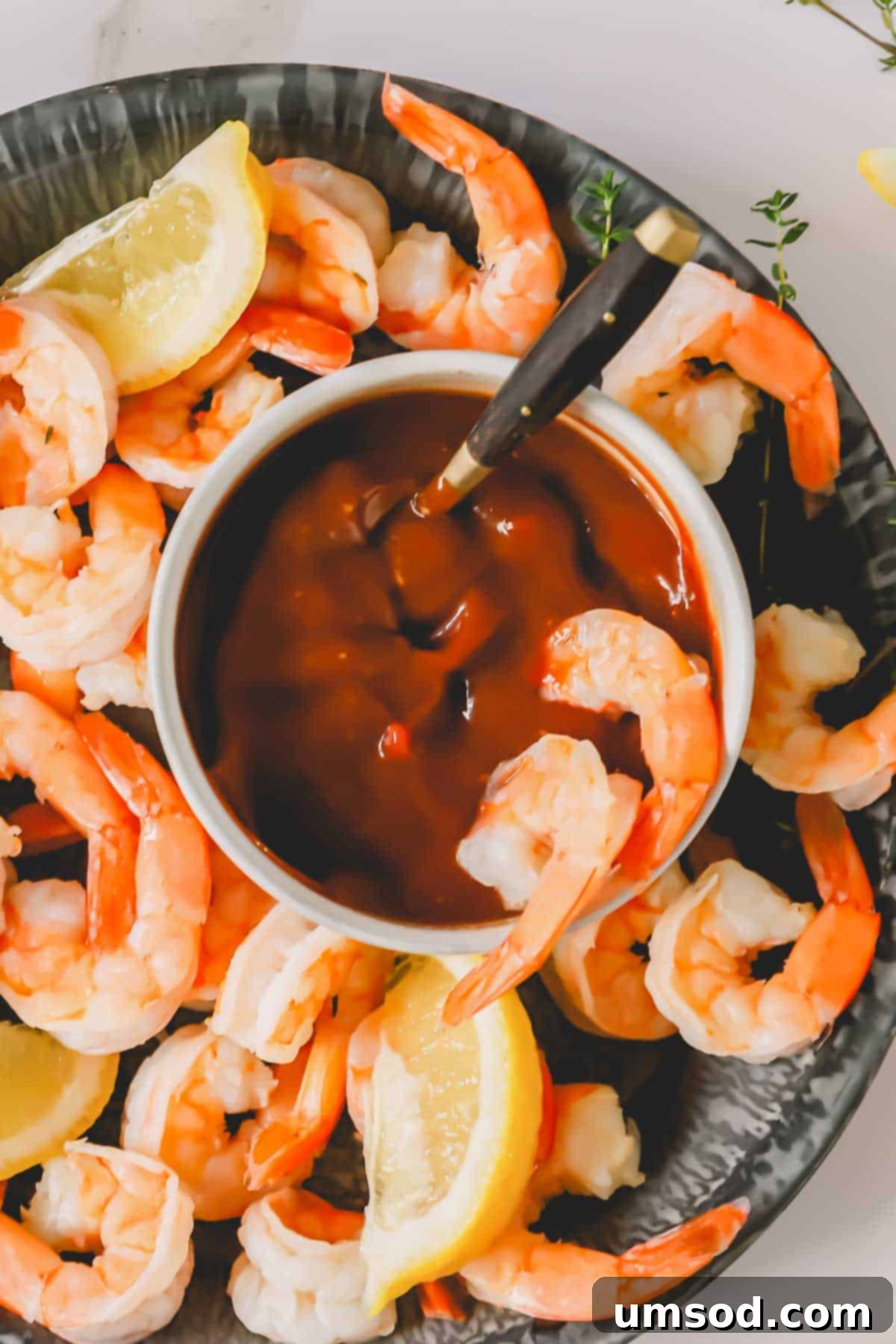 A close-up shot of two jumbo shrimp, one dipped in a small bowl of cocktail sauce, resting attractively in a larger bowl filled with more shrimp.