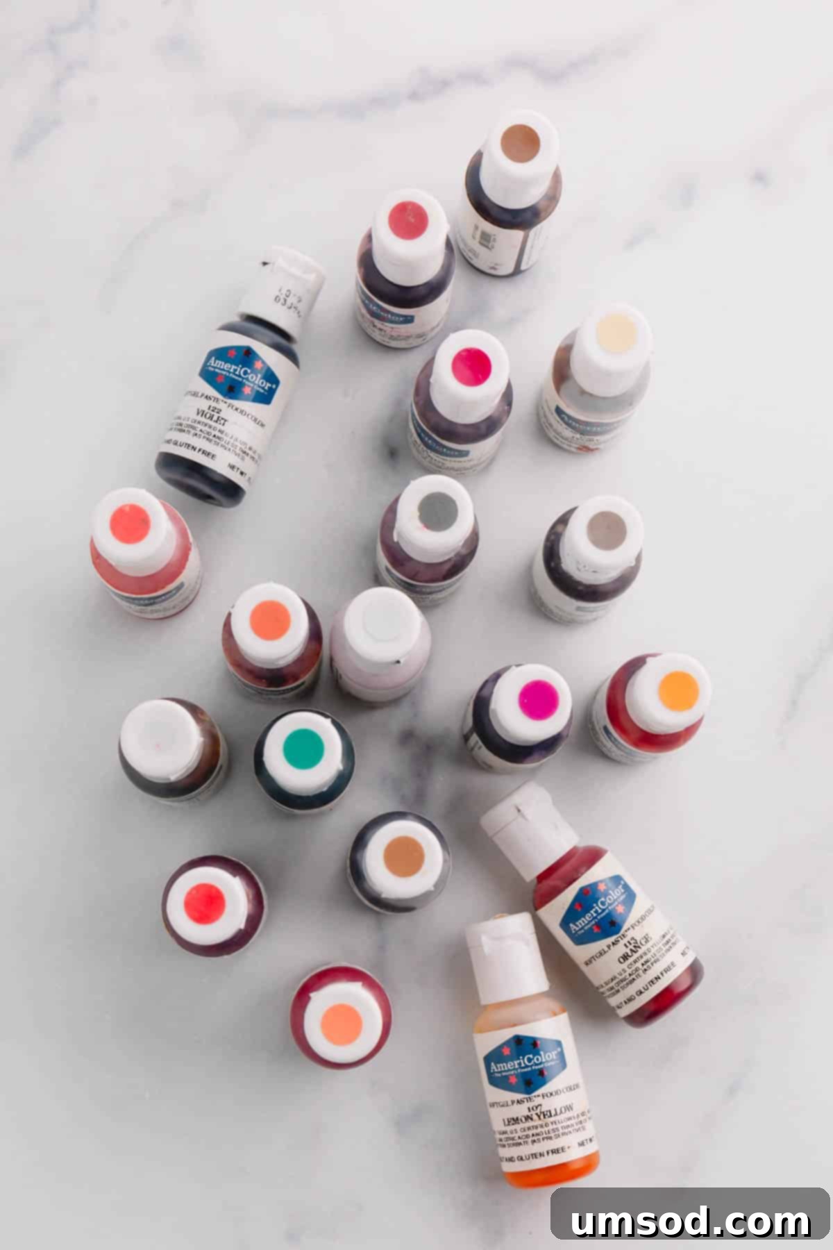 About 20 colorful Americolor brand gel food colorings on a marble background, showcasing a spectrum of vibrant hues.