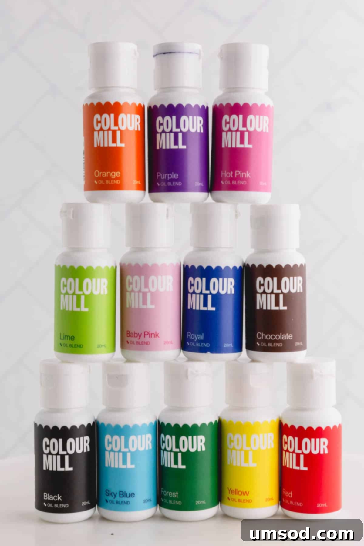 12 colorful Color Mill brand gel food colorings neatly stacked on top of each other, displaying a wide range of shades.