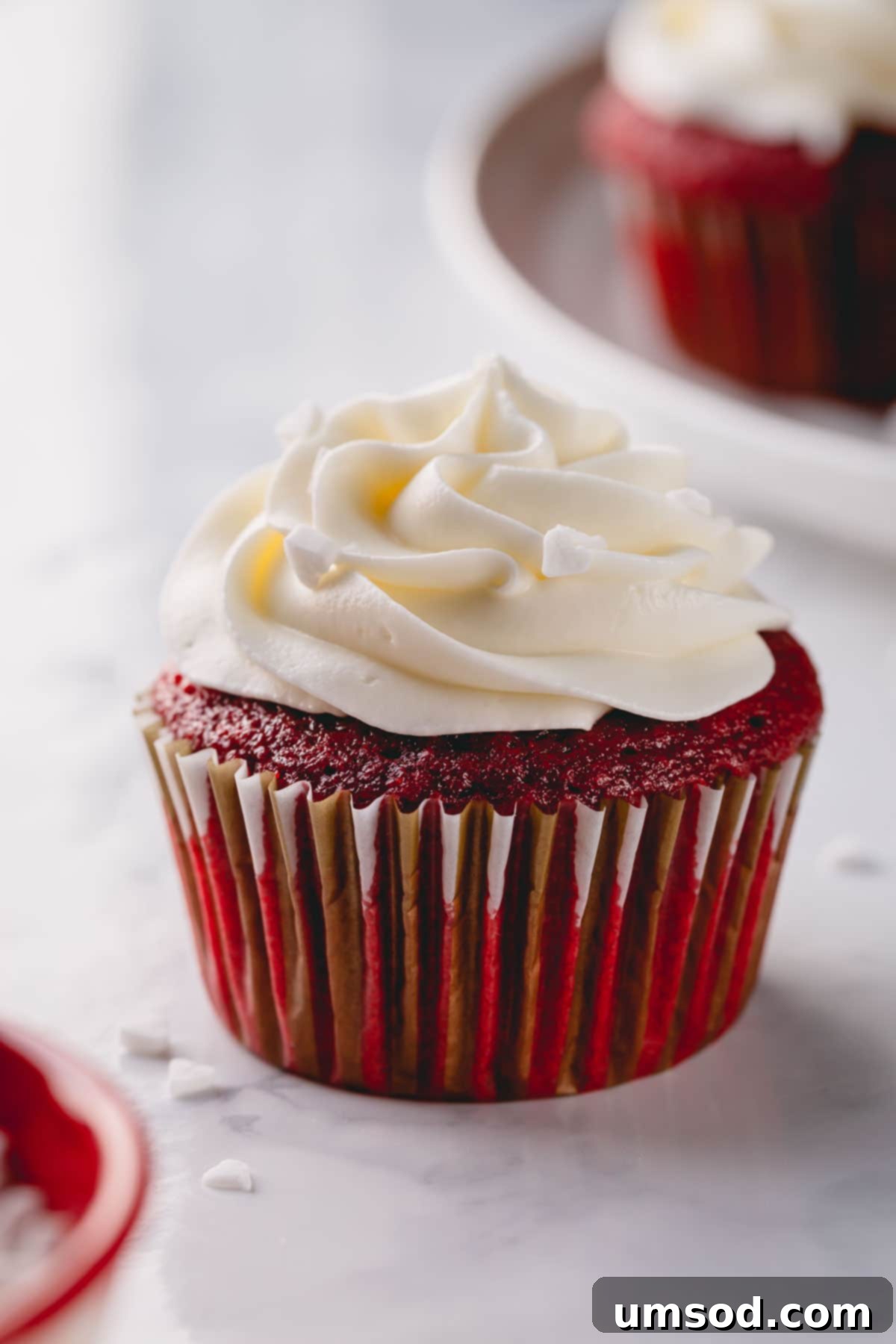 A perfectly baked red velvet cupcake topped with a generous swirl of pristine white cream cheese frosting.