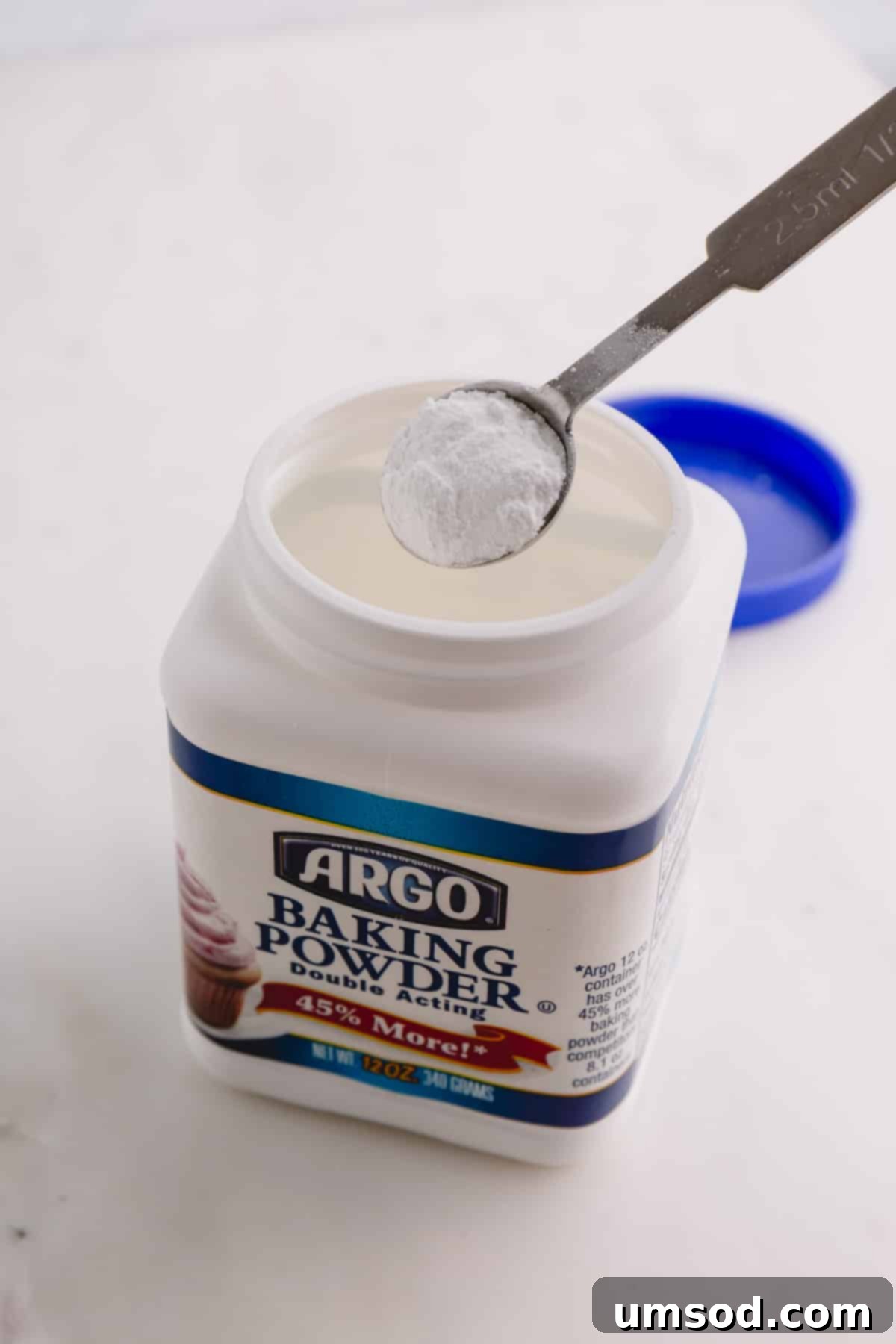 A container of baking powder with a spoonful, showing its distinct granular texture.
