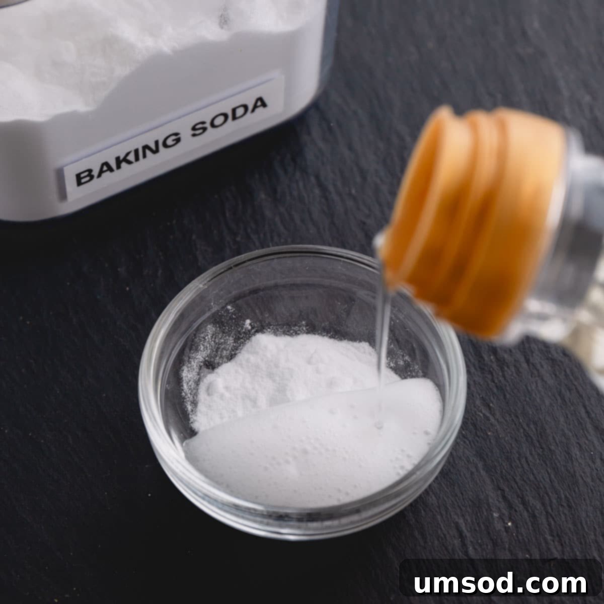 Vinegar being poured into a small glass dish with baking soda, causing the mixture to bubble up, demonstrating an active leavener.