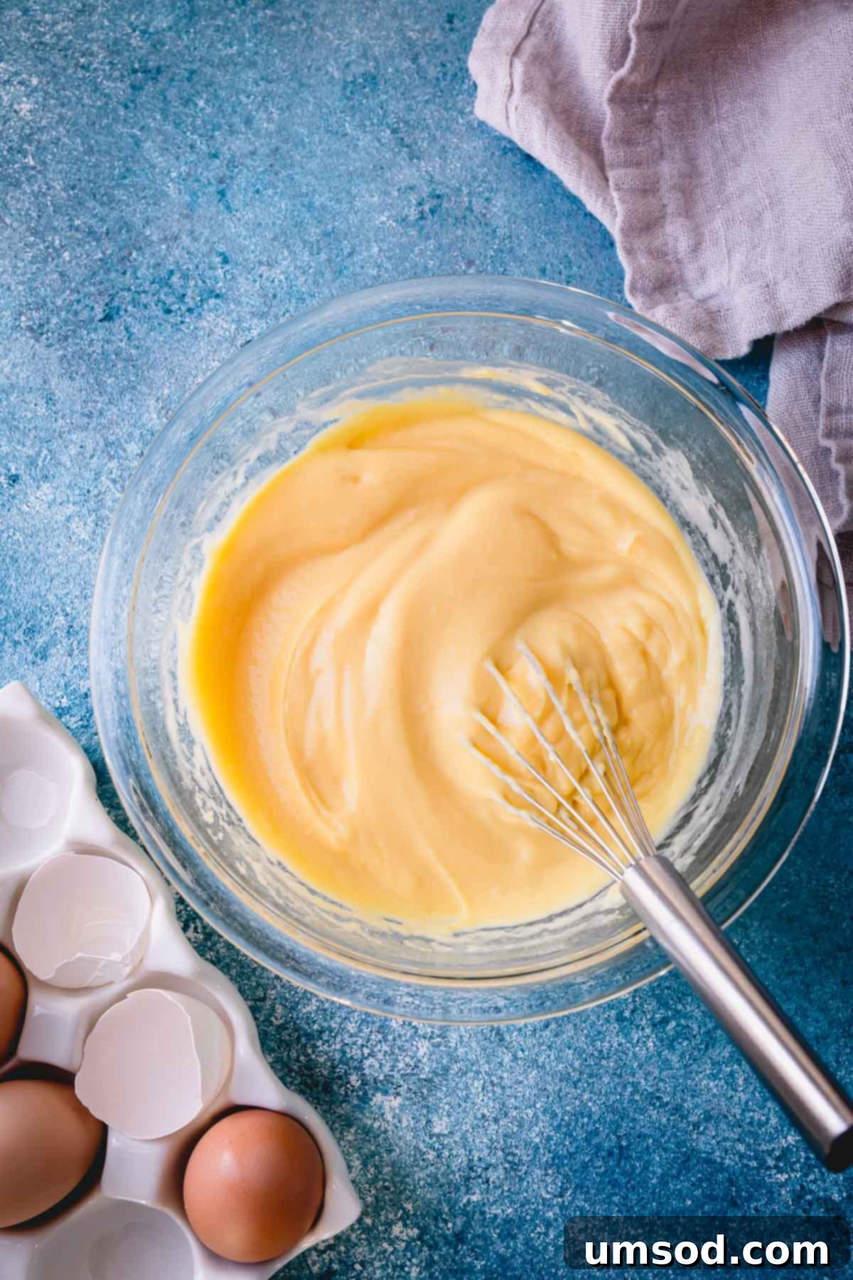 Demystifying Thickening Agents 3 Smooth, yellow pastry cream elegantly swirled in a clear glass bowl, accompanied by a whisk.