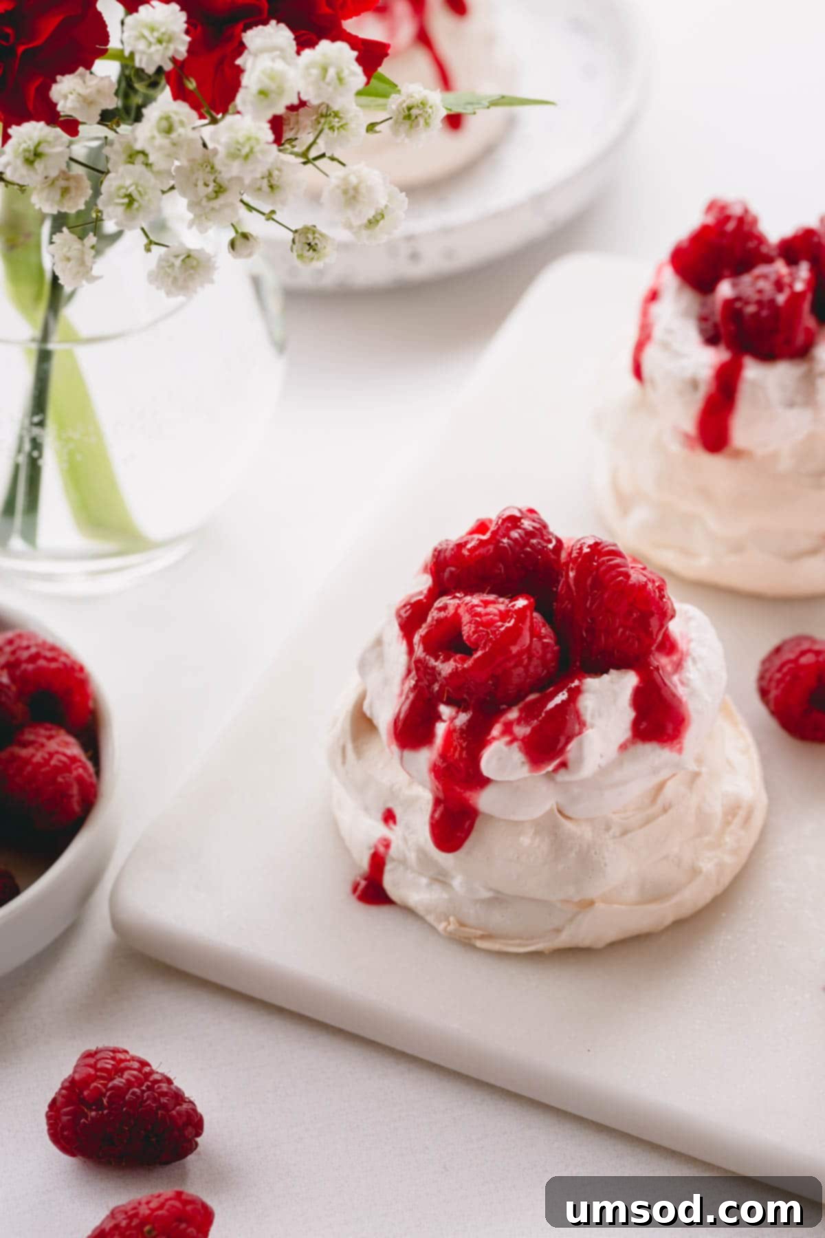 Raspberry Cloud Bites 2 Exquisite mini pavlova topped with a cloud of raspberry whipped cream, a drizzle of raspberry sauce, and fresh, vibrant raspberries.