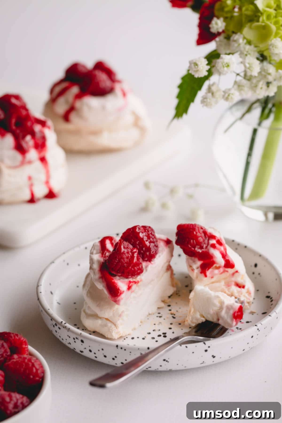 Raspberry Cloud Bites 5 A perfectly sliced mini pavlova, showcasing its crispy exterior and soft, cloud-like marshmallowy interior, adorned with raspberry whipped cream and fresh berries.