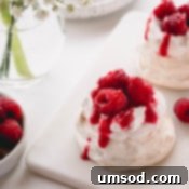 Mini pavlova topped with raspberry whipped cream, raspberry sauce and fresh raspberries.
