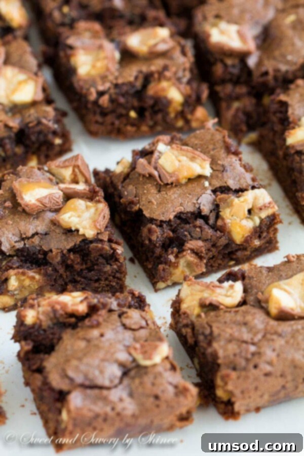 Perfectly cut fudgy Snickers brownie squares with a shiny crackle top, arranged on a crisp white surface.