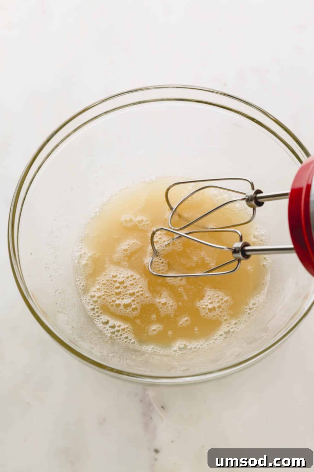 Aquafaba, sugar, cream of tartar, and salt being whipped vigorously in a bowl.