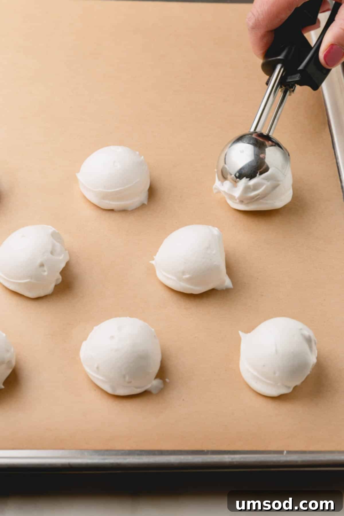 Vegan meringue being dolloped evenly onto a parchment-lined baking sheet.