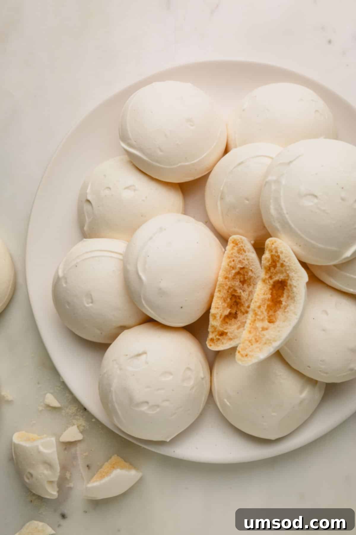 A beautifully presented plate of vegan meringue pieces, with one broken open to show its airy interior.